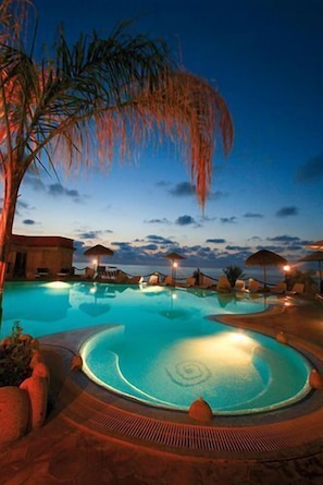 A swimming pool with a circular hot tub area, surrounded by lounge chairs and umbrellas, under a twilight sky. - Baia Tropea Resort (Parghelia)