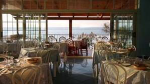 A dining area with tables set for service, large windows offering a view of the sea, and a covered outdoor seating area. - Baia Tropea Resort (Parghelia)
