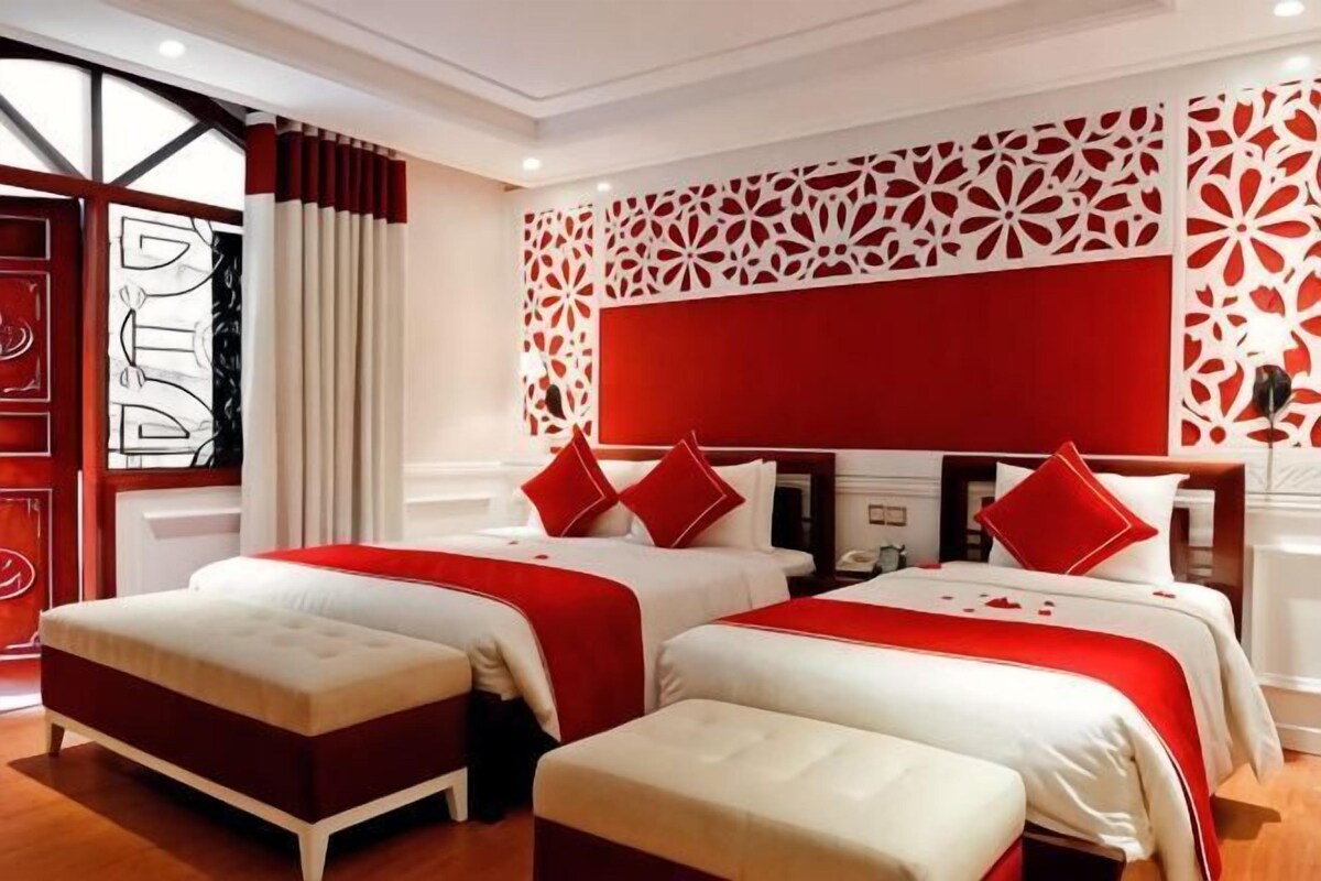 Une chambre d’hôtel avec deux lits, une décoration aux couleurs rouge et blanche, et un motif décoratif sur le mur.