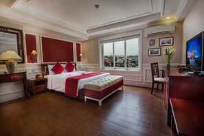 Ein Hotelzimmer mit einem großen Bett, einem Fernseher, einem Schreibtisch und einem Fenster mit Blick auf die Stadt.