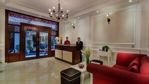 Een hotellobby met een receptiebalie, een rode bank, een kroonluchter en een decoratief wandpaneel.