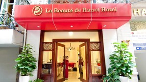 De ingang van Hotel La Beauté de Hanoi, met een rode luifel en twee potplanten aan weerszijden.
