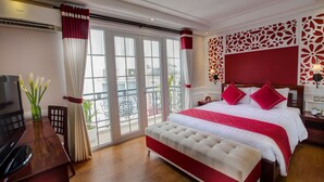 Een hotelkamer met een groot bed, een bureau met televisie, een balkon met uitzicht en een decoratief wandpaneel.