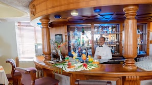 Una zona de bar con taburetes de madera, un cantinero y una variedad de botellas y vasos en estanterías.