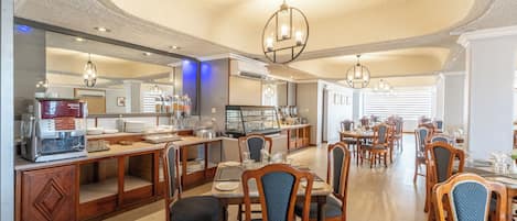 Un comedor de hotel con mesas y sillas de madera, una estación de buffet y un espejo grande.
