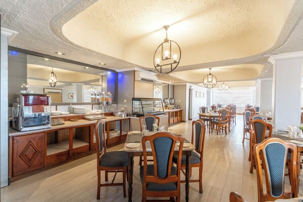 A hotel dining area with wooden tables and chairs, a buffet station, and a large mirror. - Gold Crest Hotel (Quatre Bornes)