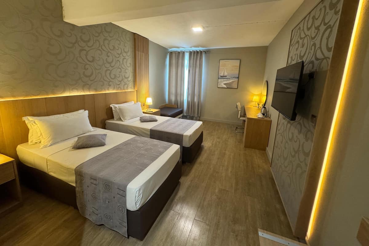 A hotel room with two beds, a desk, a TV, and a painting on the wall.