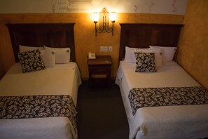 A hotel room with two single beds, each with floral-patterned bedding, a nightstand with a phone, and a wall-mounted light fixture. - Hotel Historia (Morelia)