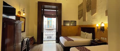 A hotel room with two beds, a wooden wardrobe, a desk, and a chandelier.