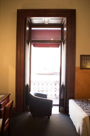 A hotel room with a bed, a chair, a desk, and a view of a balcony with a railing. - Hotel Historia (Morelia)