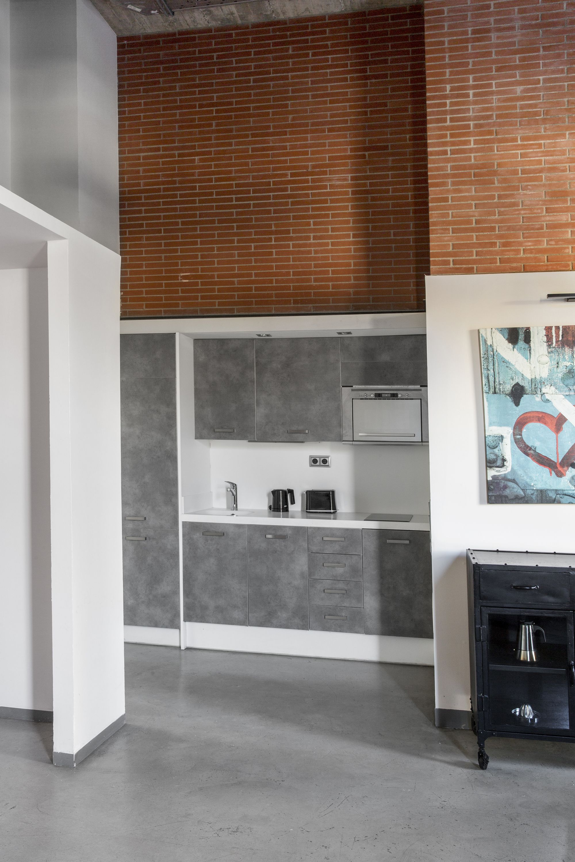 Una cocina moderna con gabinetes grises, una encimera blanca y un mueble negro con una tetera.