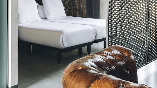 A room with a bed, a leather ottoman, a metal partition, and a hanging light fixture. - Aparthotel República (Barcelona)