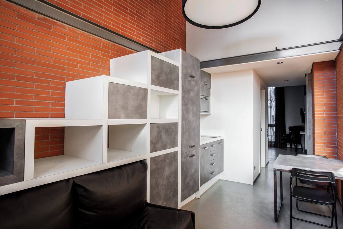 A modern kitchen with a brick wall, white cabinetry, and a dining area with a table and chairs.