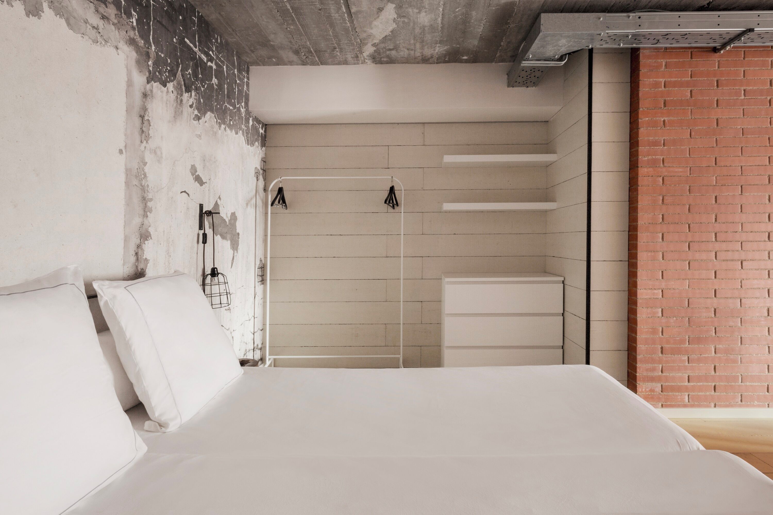 Une chambre à coucher avec un lit, une armoire blanche et un mur en briques.