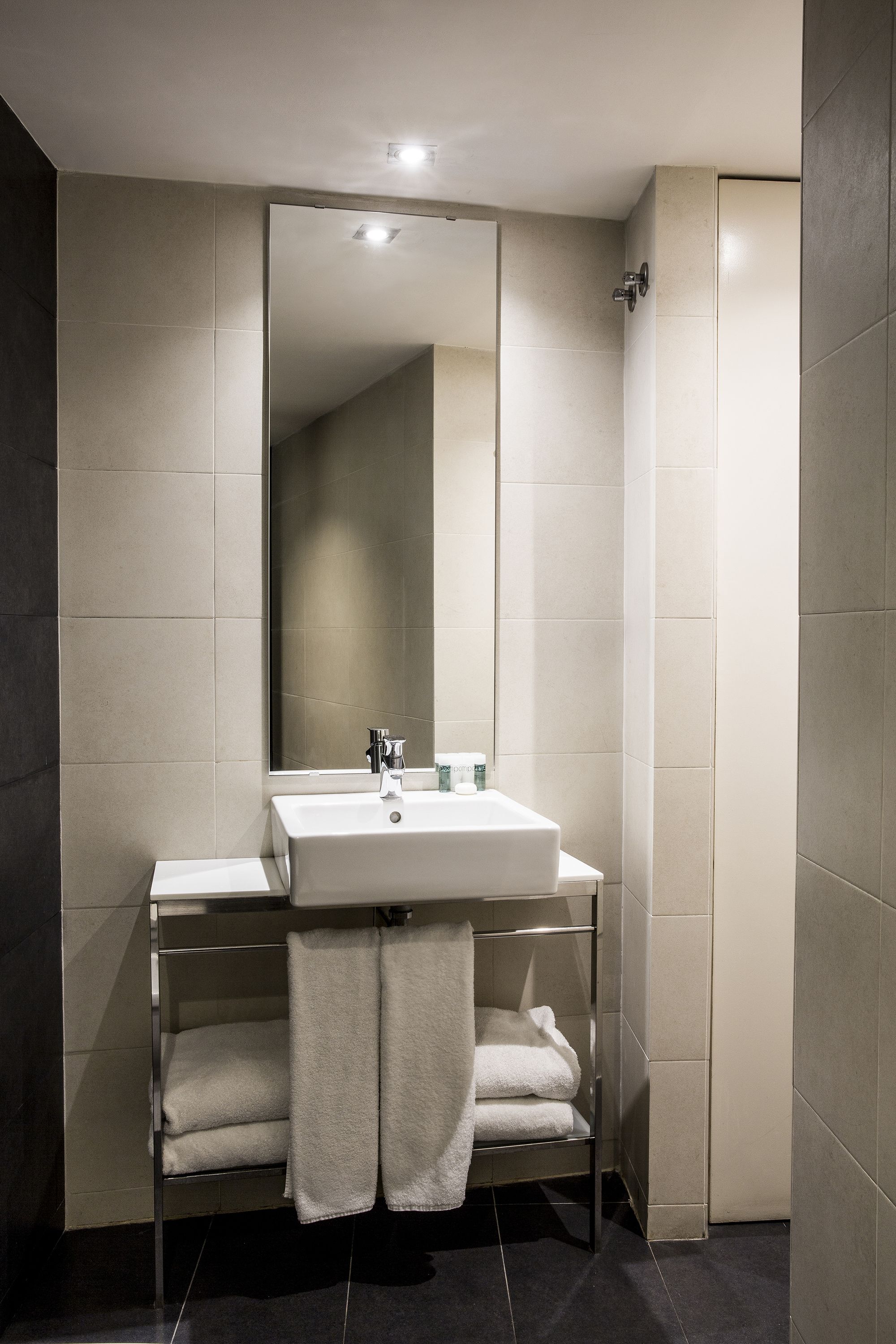 Un baño moderno con un lavamanos blanco, un espejo y un perchero para toallas.