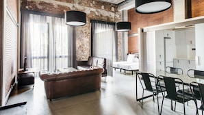 A modern interior with a leather sofa, dining table, and chairs, a brick wall, and large windows with curtains. - Aparthotel República (Barcelona)