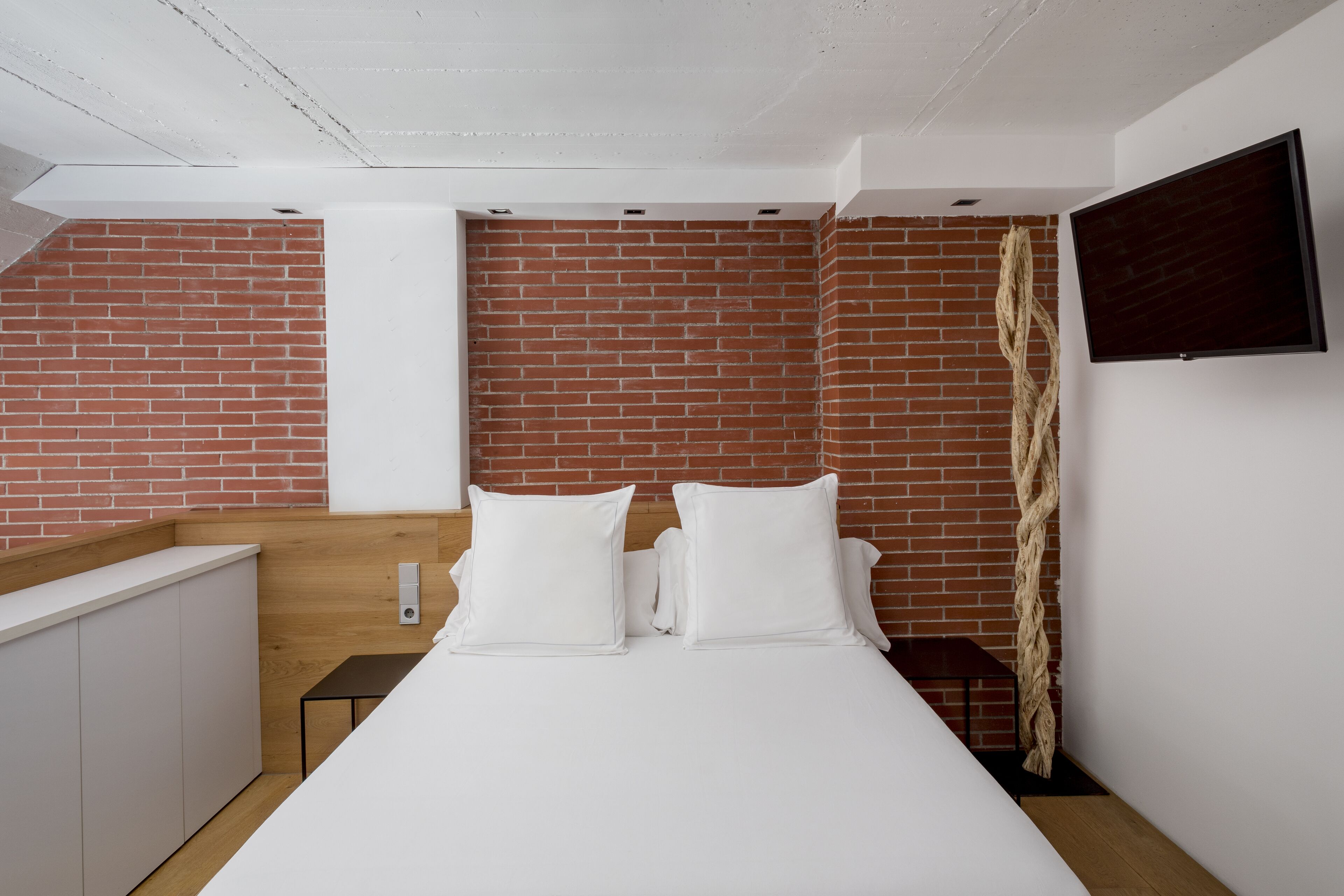 Un dormitorio moderno con pared de ladrillo, televisor de pantalla plana y cabecero de madera.