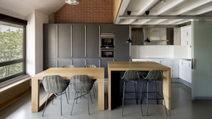 A modern kitchen with a wooden table and chairs, a brick wall, and a large window. - Aparthotel República (Barcelona)