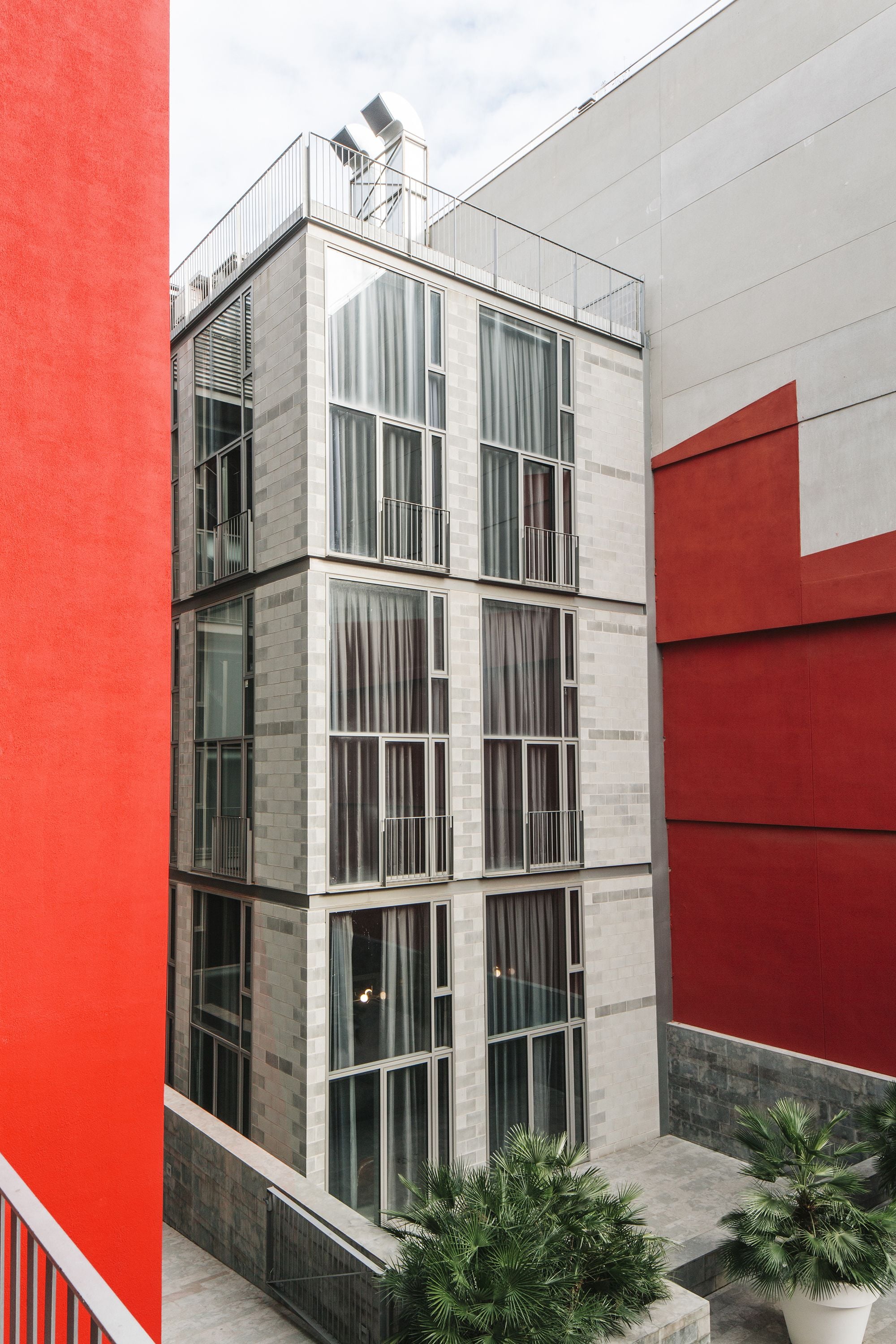 Een modern gebouw met een rood-grijs gevelontwerp, grote ramen en een balkon.
