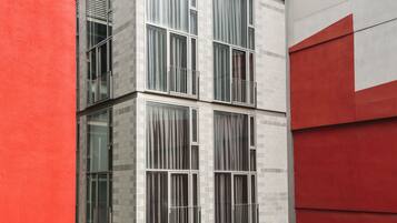 A modern building with a red and grey facade, large windows, and a balcony.