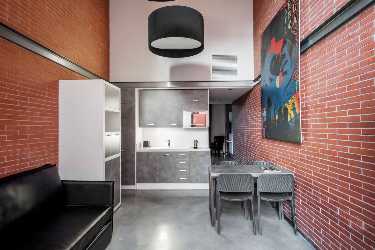 A modern kitchen with a grey countertop, a black hanging light fixture, and a red brick wall.