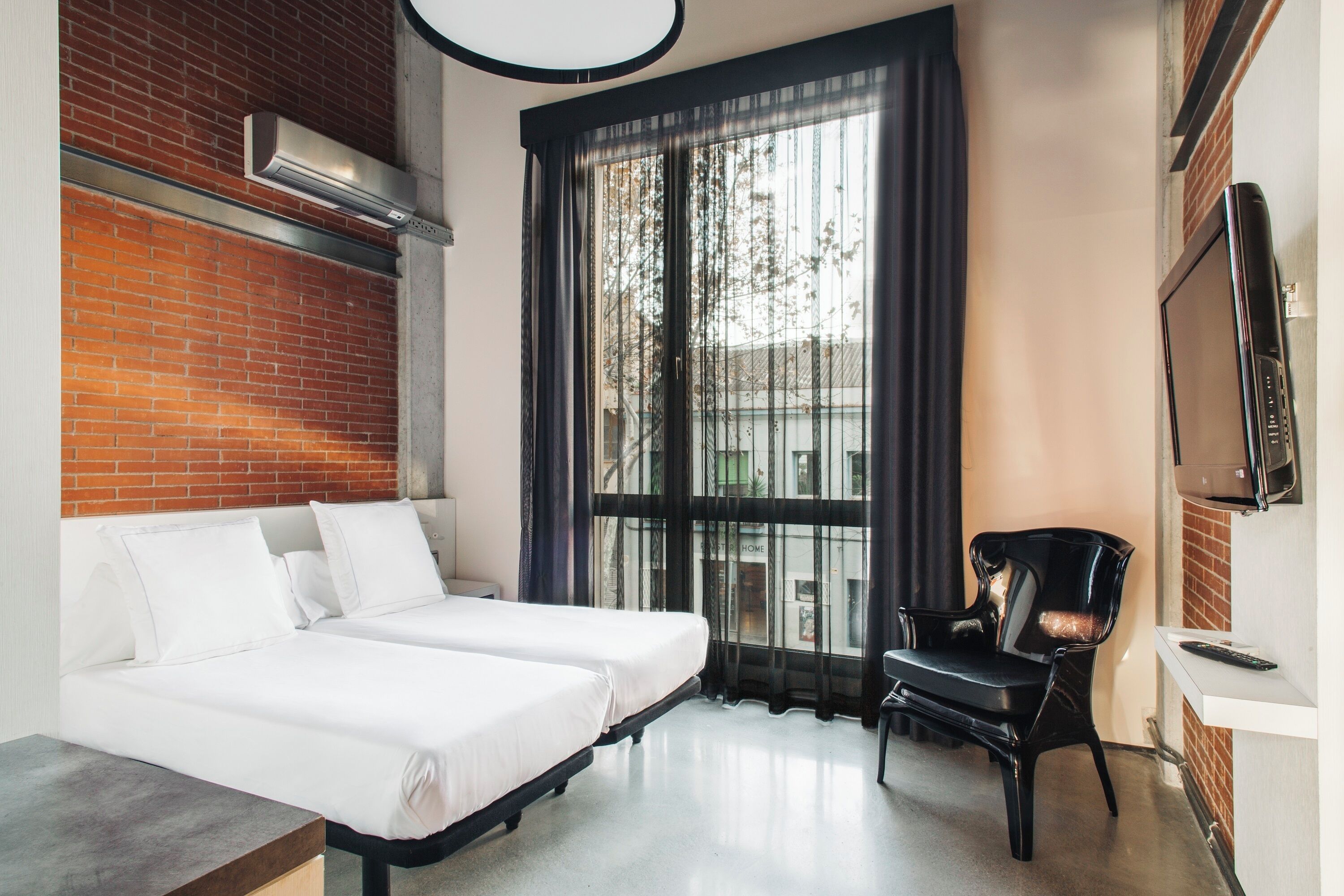 Ett hotellrum med två sängar, en svart stol, en tv och ett stort fönster med gardiner.