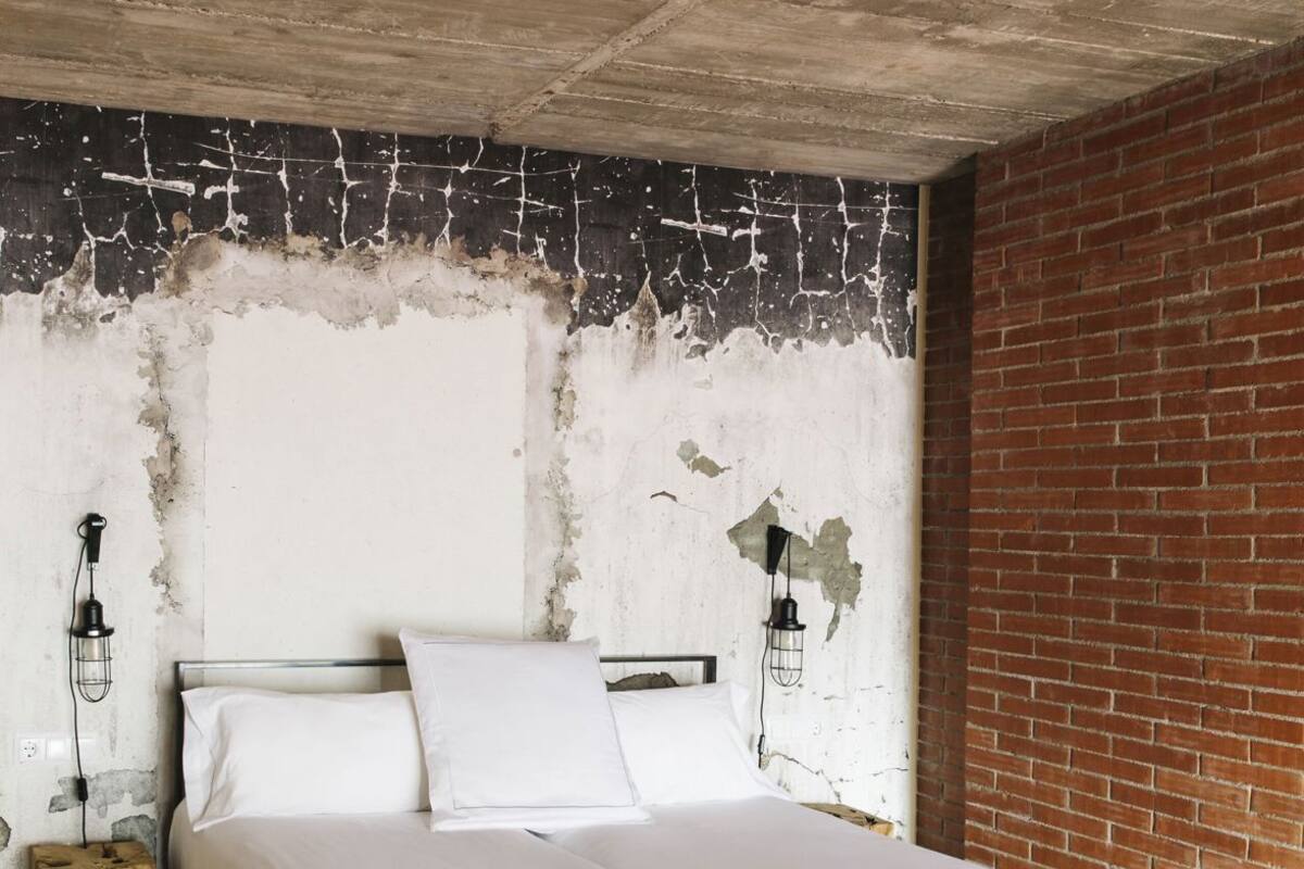 A bedroom with a bed, white bedding, a brick wall, and exposed ceiling beams.