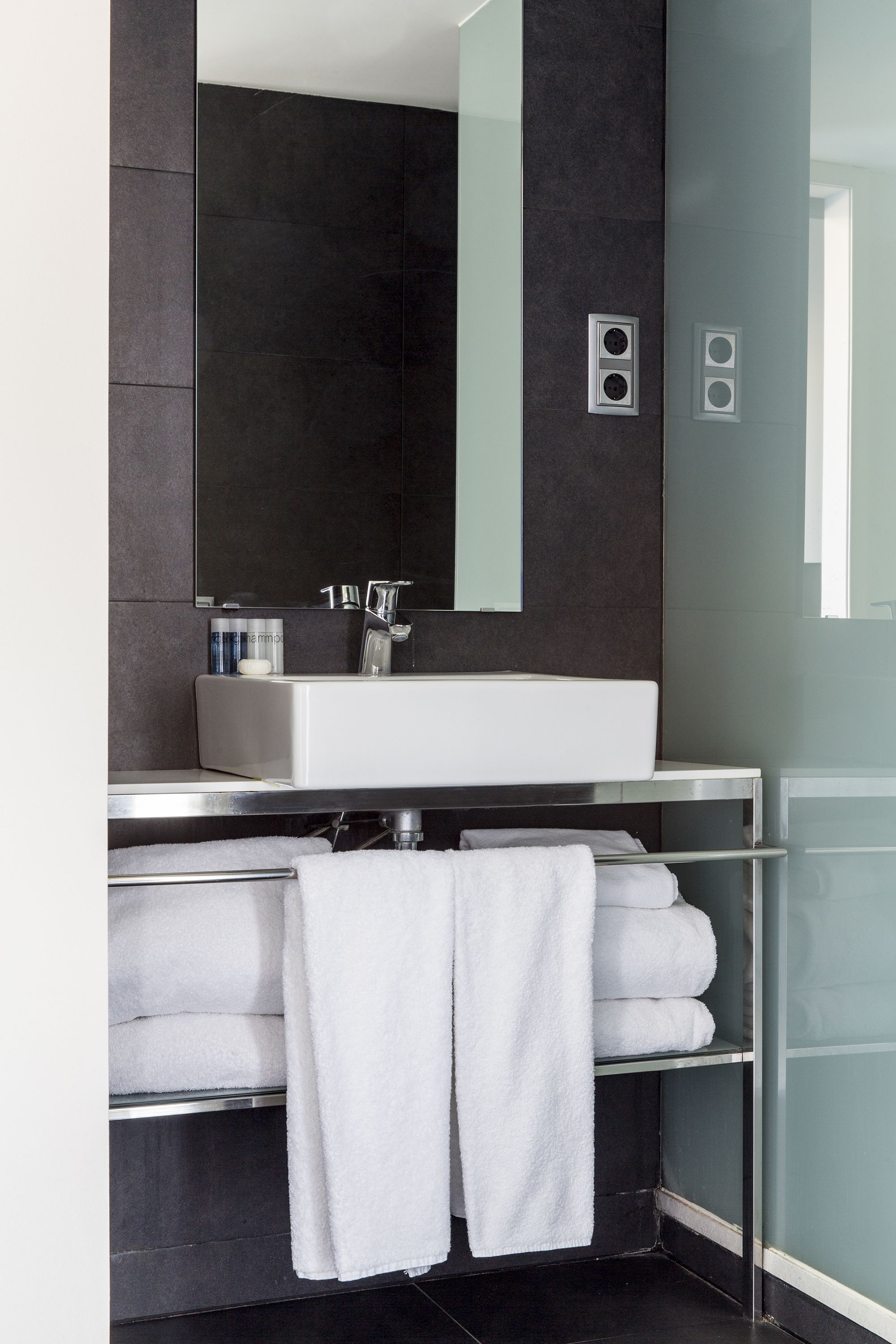 A modern bathroom with a large mirror, a white sink, and a towel rack.
