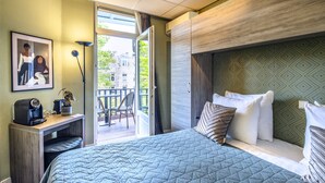 Habitación de hotel con una cama grande, un escritorio con cafetera y vistas al balcón exterior.