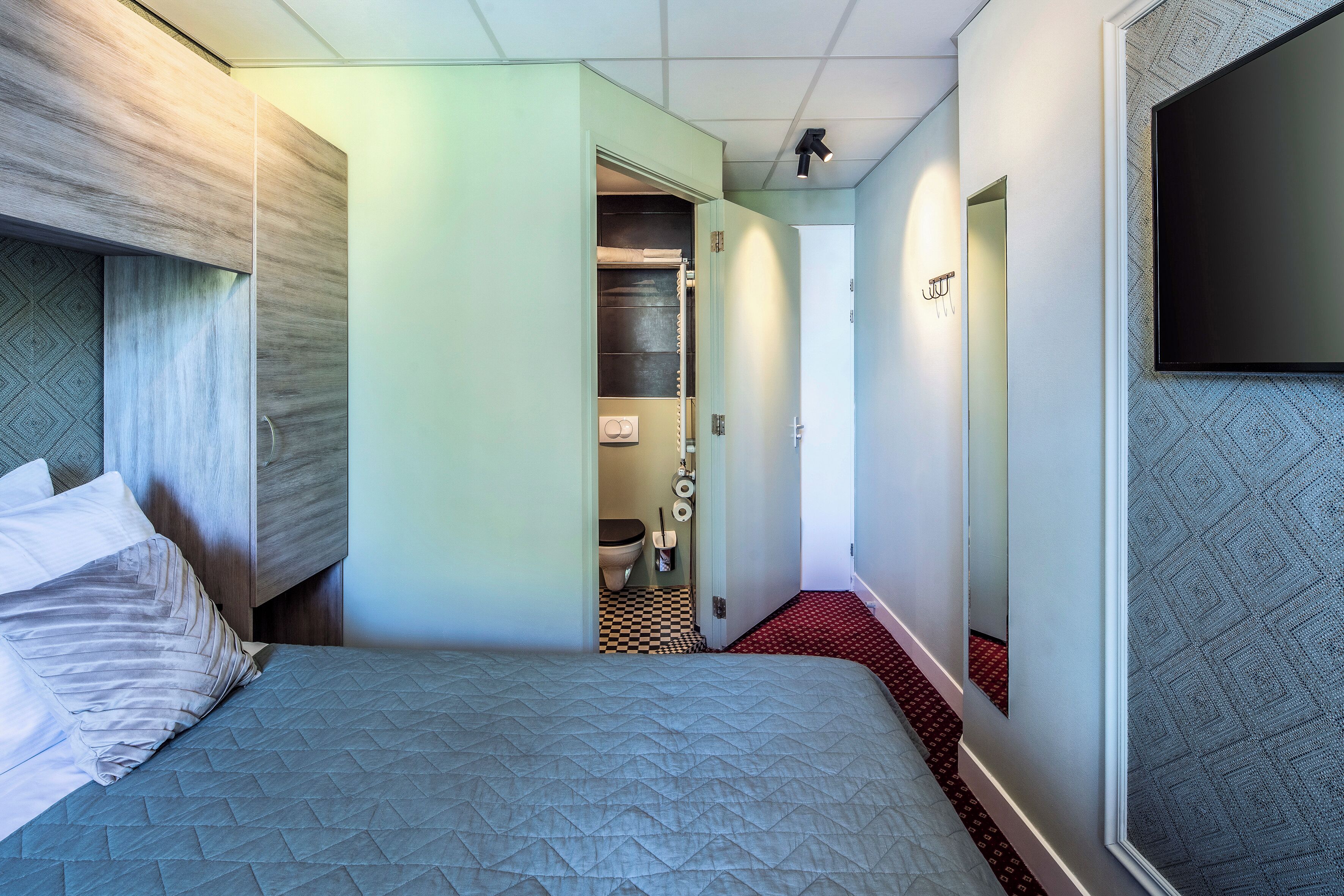 A hotel room with a bed, a wardrobe, a bathroom, and a TV mounted on the wall.