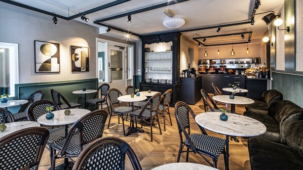Interior de restaurante con mesas redondas, sillas de mimbre y una zona de bar.