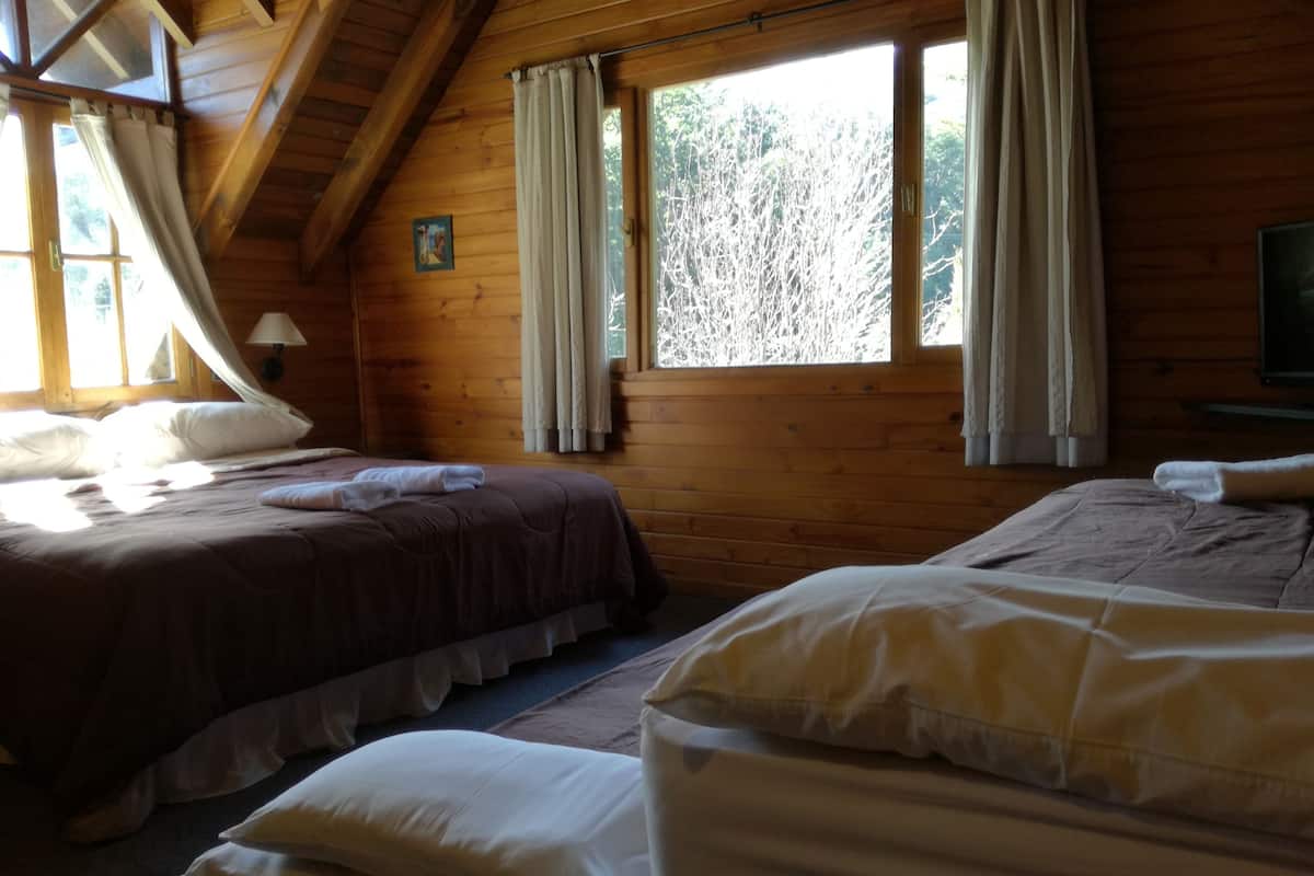 A cabin with two beds, wooden walls, a ceiling fan, and large windows with curtains.