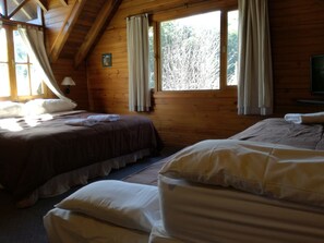 Una cabaña con dos camas, paredes de madera, ventilador de techo y ventanas grandes con cortinas.