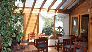 A wooden cabin with a dining area featuring wooden tables and chairs, a potted plant, and a view through a window. - Portal de Piedra (Villa La Angostura)