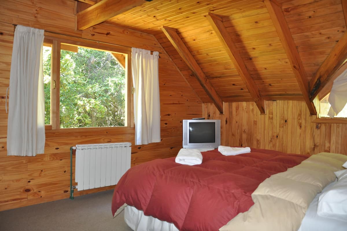 A wooden cabin bedroom with a bed, a television, and a window with curtains.