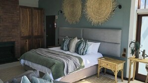 A modern bedroom with a large bed, a fireplace, and a dining area. - Shaloha Guesthouse on Supertubes (Jeffreys Bay)