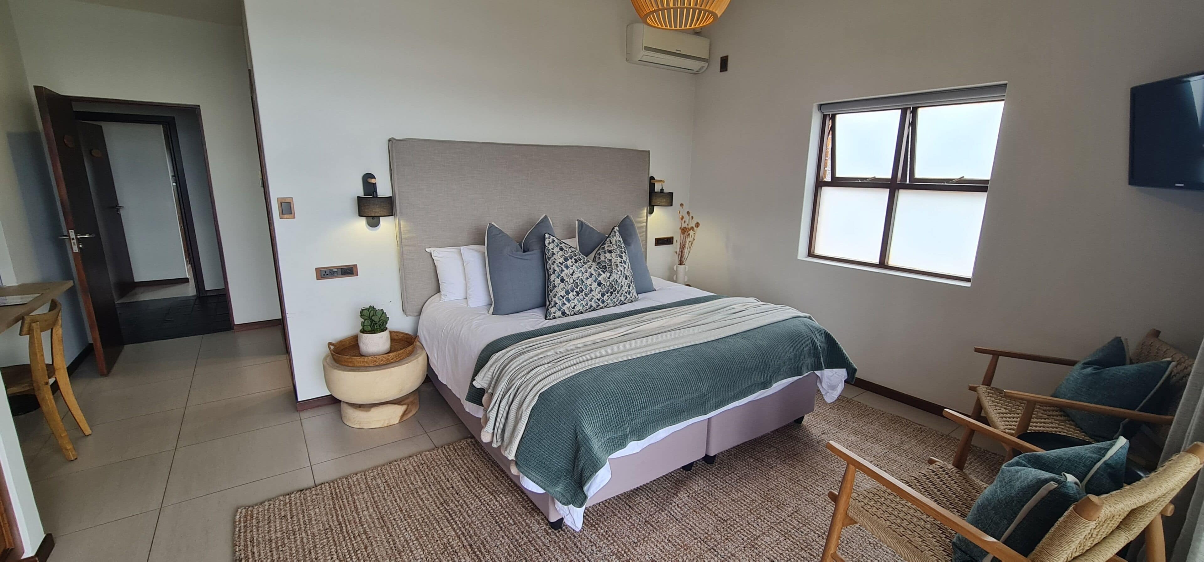 A bedroom with a bed, bedside tables, a chair, a window, and an air conditioning unit.