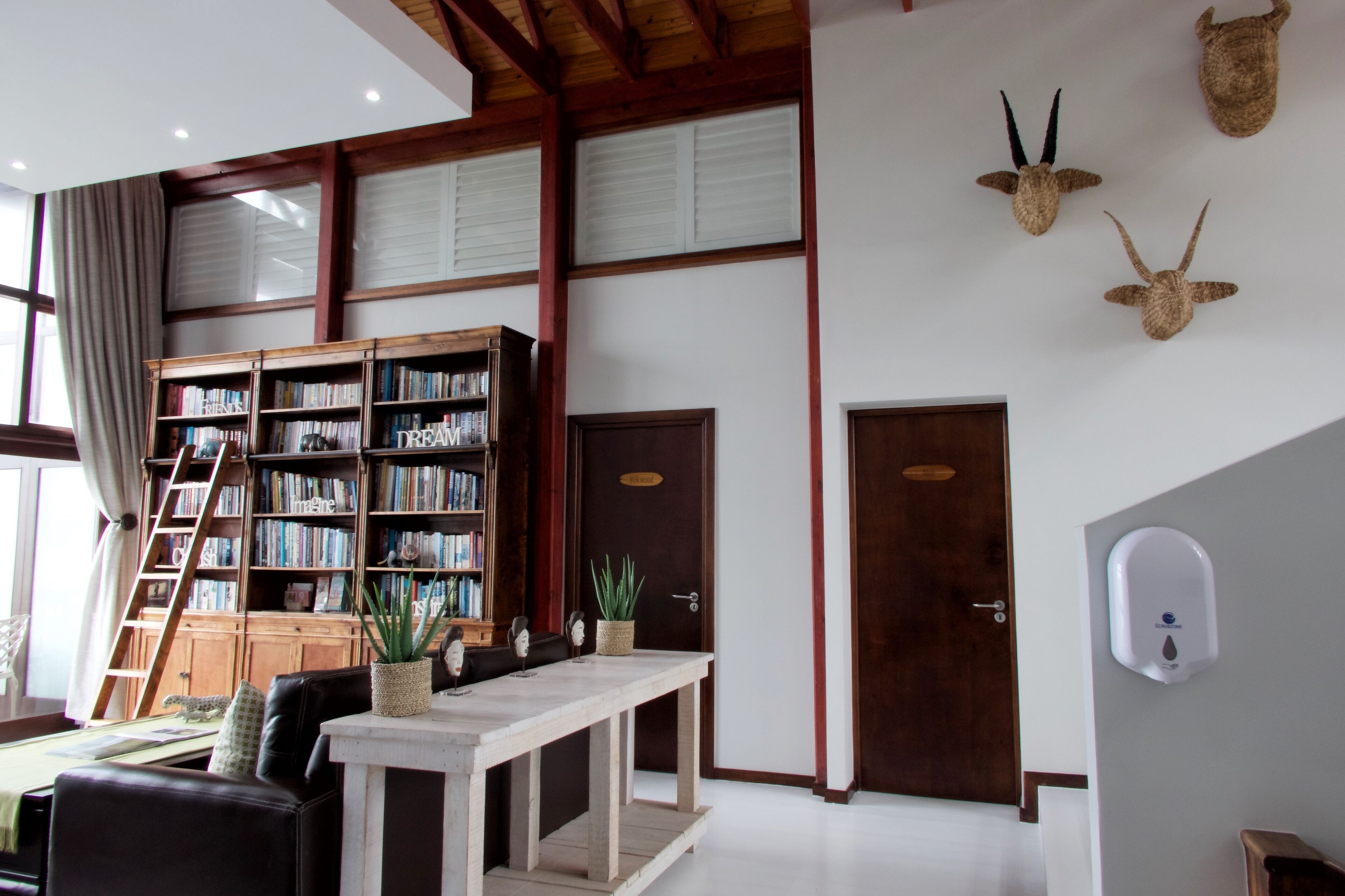Un salon spacieux avec une grande bibliothèque, une table en bois et un canapé confortable. Il y a deux portes et un distributeur de gel hydroalcoolique fixé au mur.