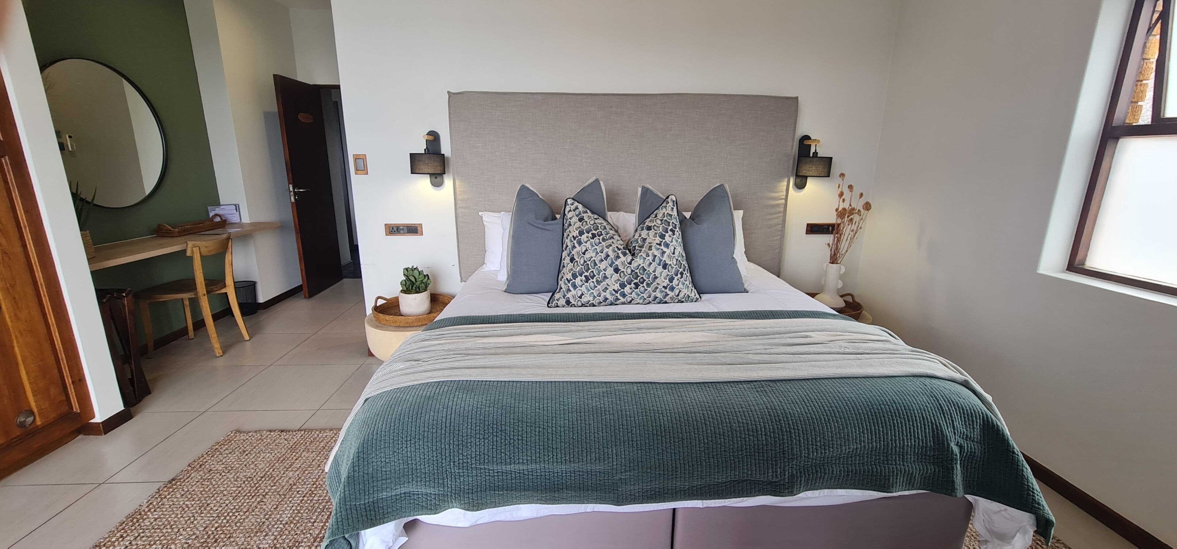 A bedroom with a bed, bedside tables, a mirror, and a door.