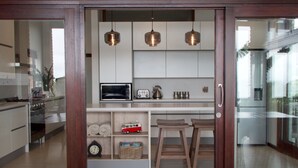 A modern kitchen with white cabinets, a microwave, a toaster, and hanging pendant lights. - Shaloha Guesthouse on Supertubes (Jeffreys Bay)