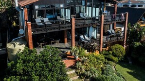 A two-story building with a balcony, outdoor seating, and a garden. - Shaloha Guesthouse on Supertubes (Jeffreys Bay)