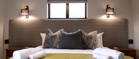 A neatly made bed with a patterned headboard, two bedside lamps, and a window above.