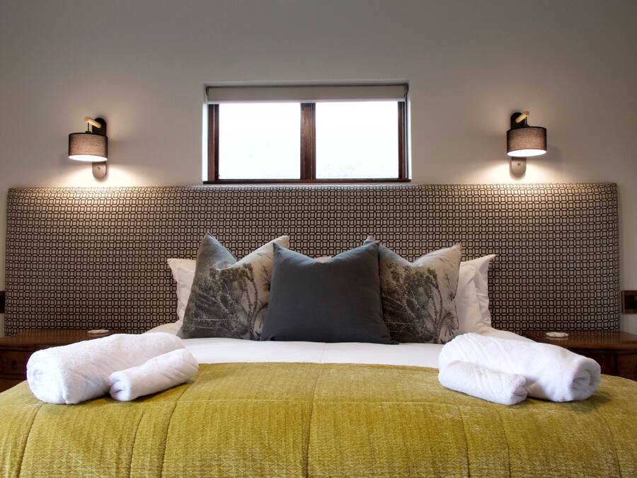 Una cama bien hecha con un cabecero estampado, dos lámparas de noche y una ventana arriba.