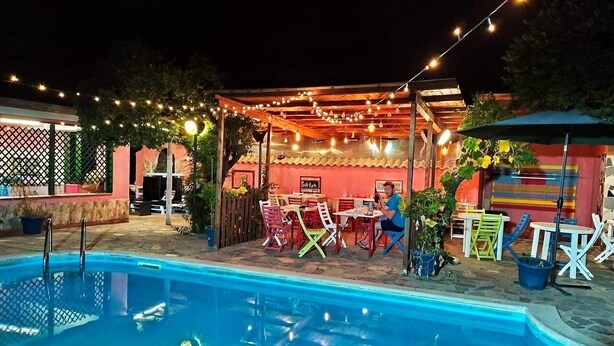 Un área junto a la piscina con zona de estar cubierta, luces colgantes y mobiliario de exterior.