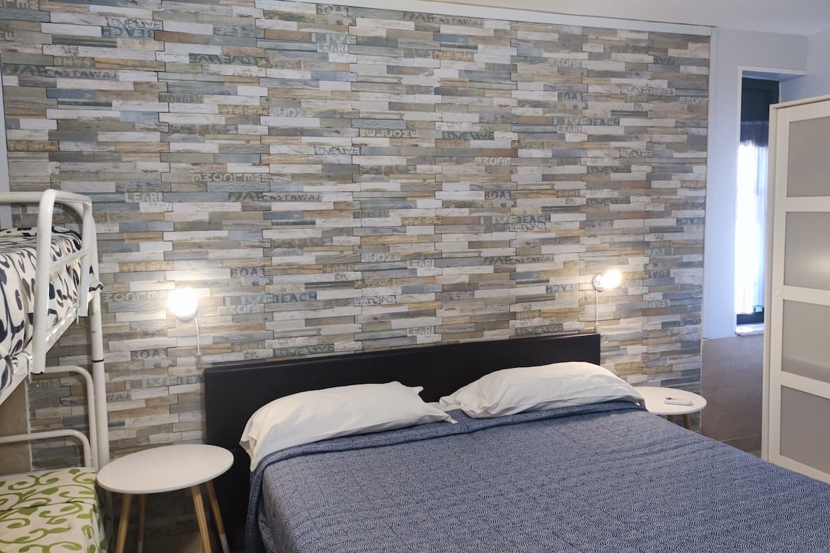 A bedroom with a bed, a bunk bed, a bedside table, and a wall with a mosaic pattern.