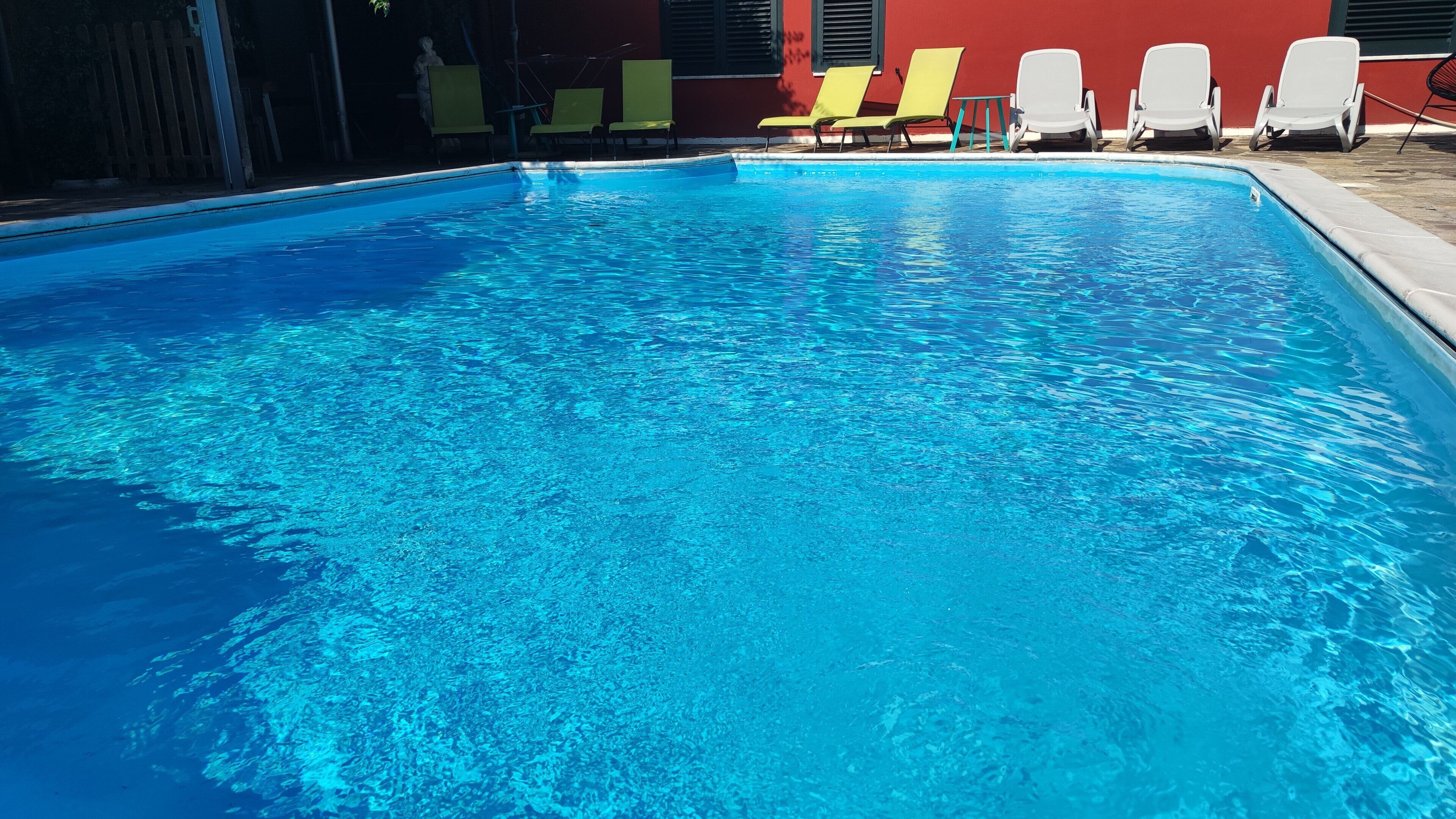 A swimming pool with clear blue water, surrounded by yellow and white lounge chairs.
