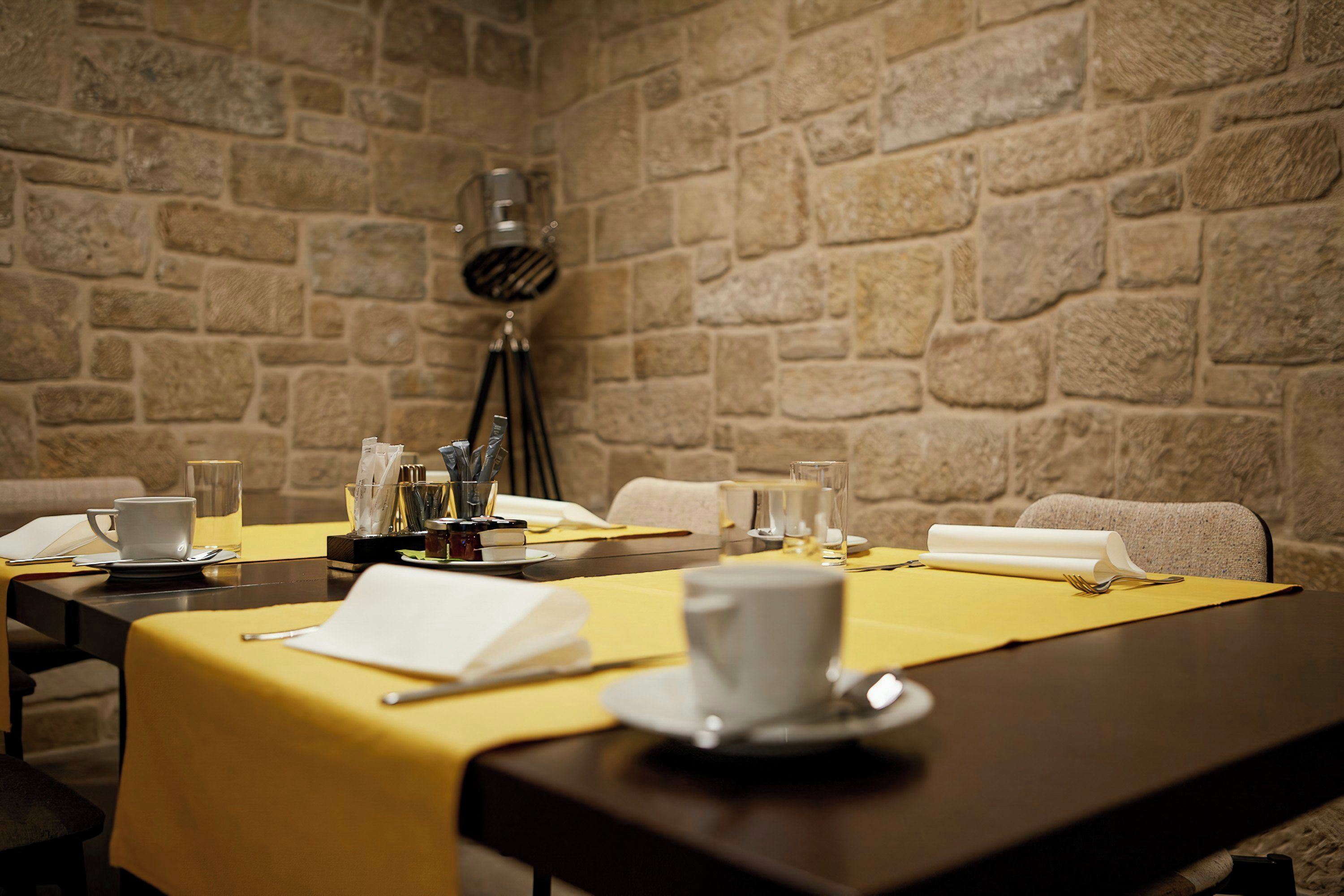 A conference room with a stone wall, a table set with a yellow tablecloth, and a tripod-mounted lamp.