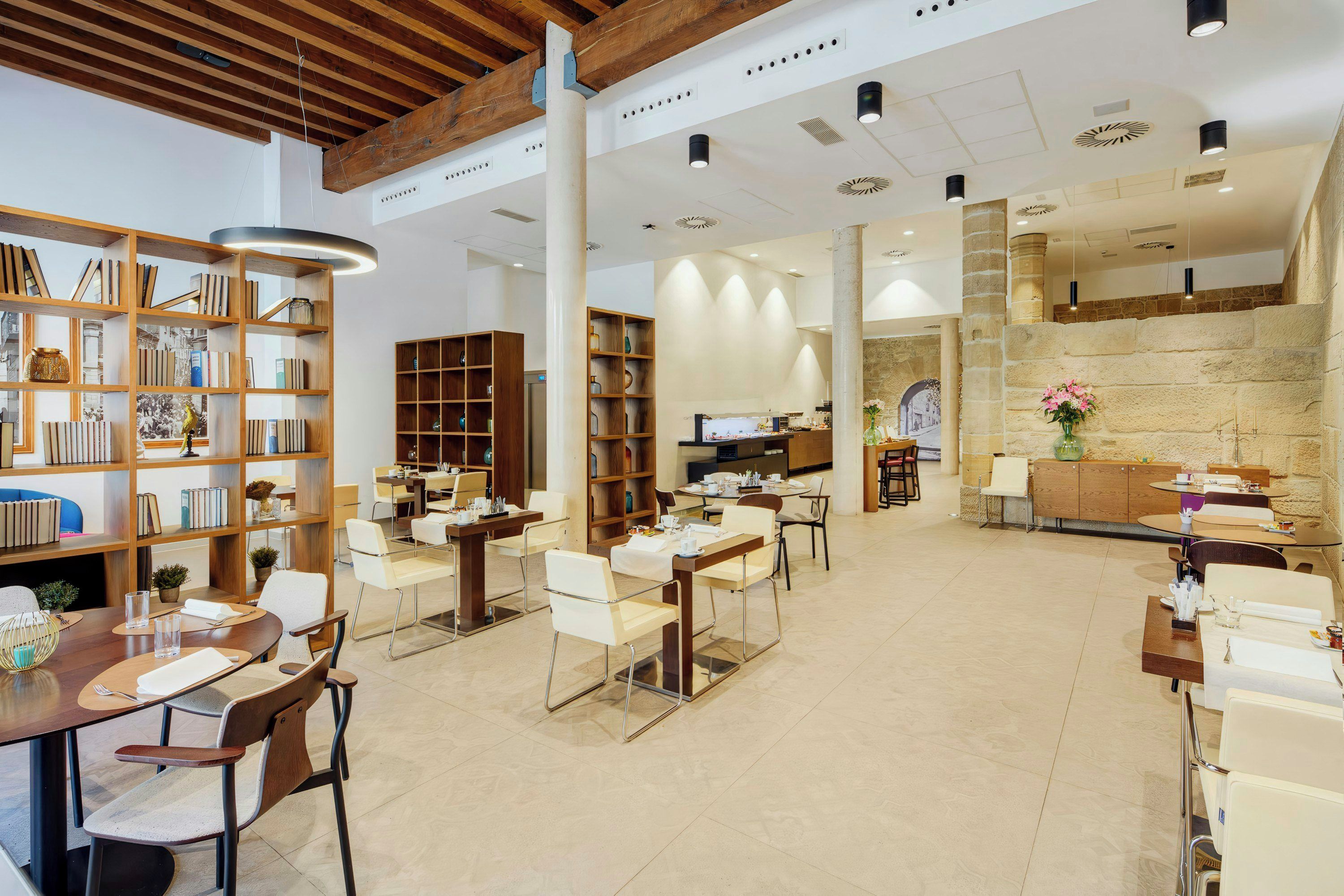 Una biblioteca amplia con varias zonas de estar, estanterías y una pared de piedra.