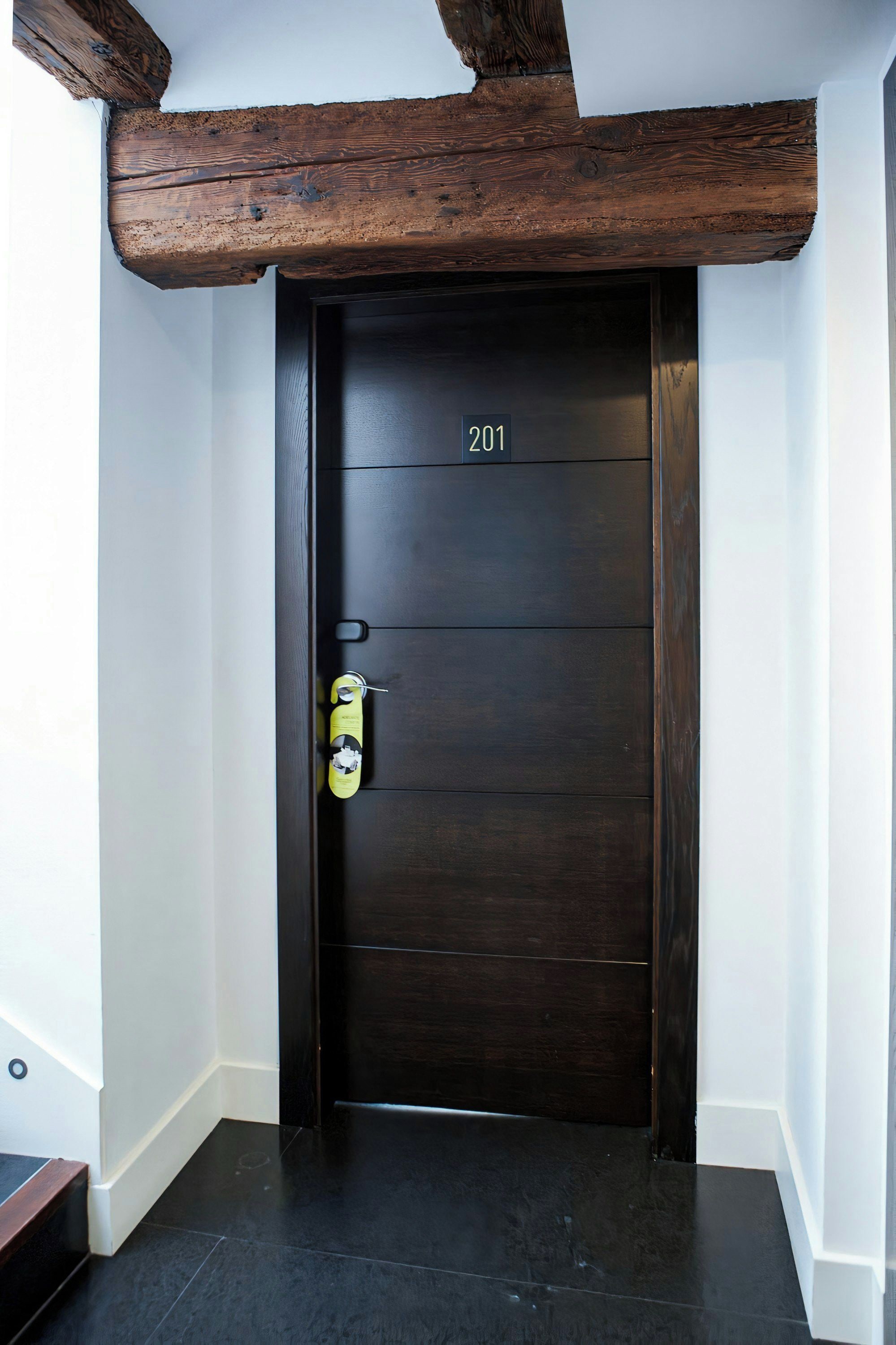 Una puerta de madera oscura con una placa de número, un timbre y una mirilla.