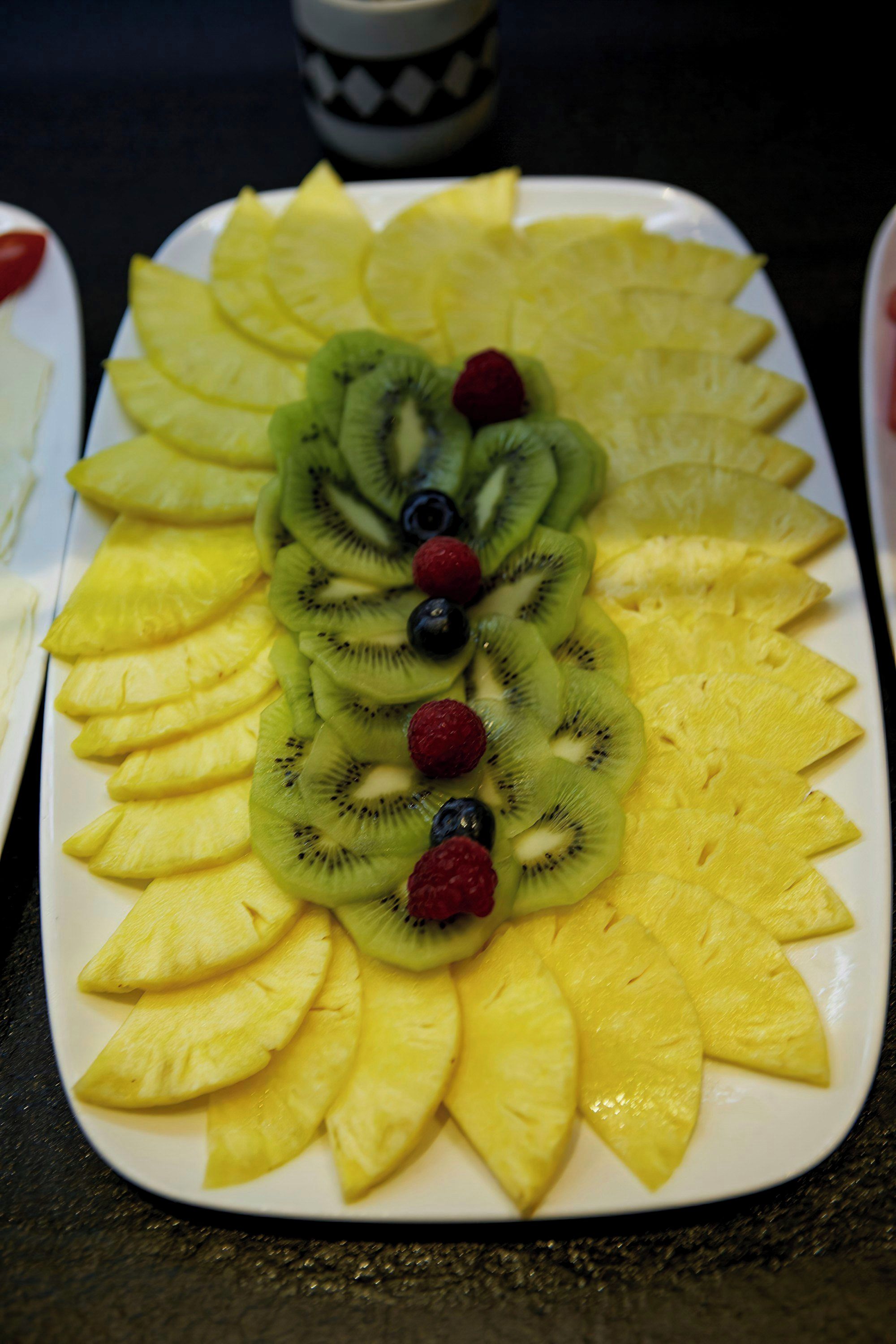 Une assiette de fruits disposés en cercle, avec des tranches d’ananas, de kiwis et des baies.